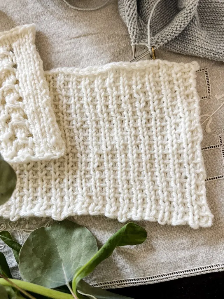 A close-up showing a white knit swatch with slipped stitches with yarn held in front.