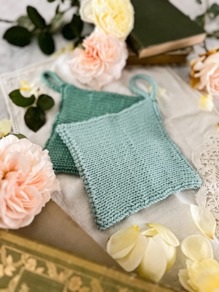 A side angle photograph of a seafoam green handknit potholder sitting on top of a darker teal potholder.