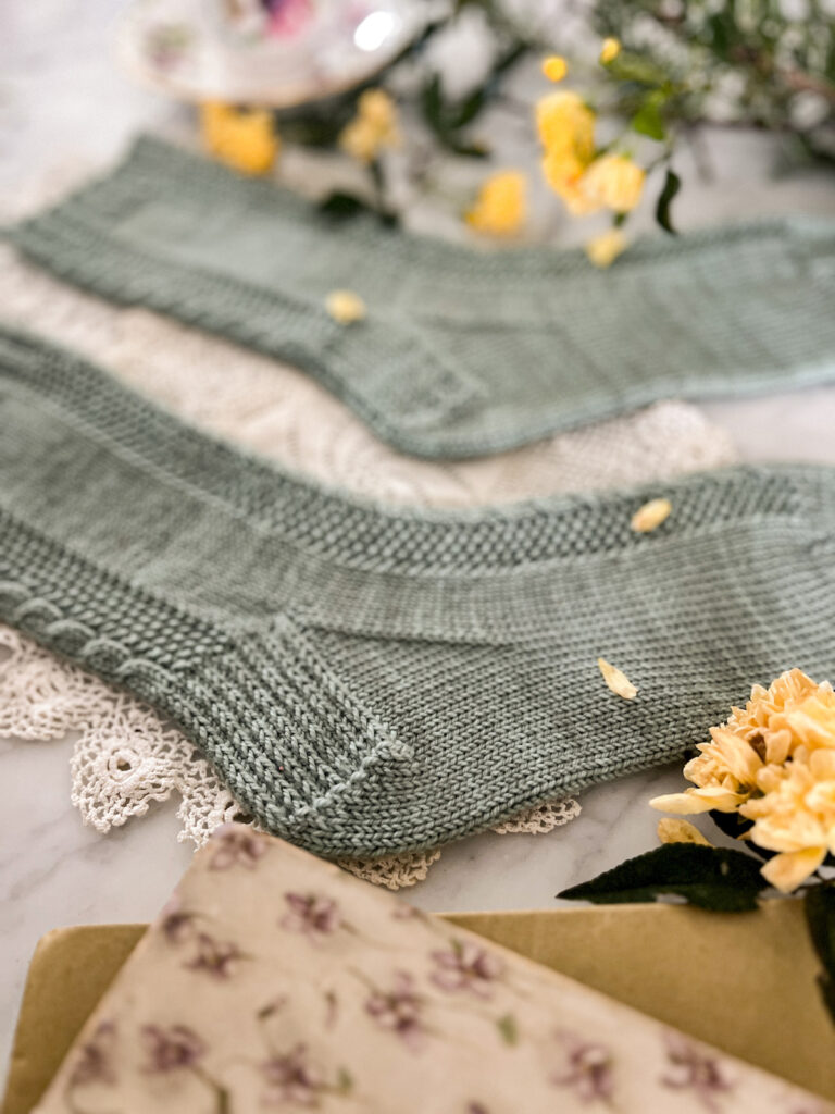 A close up on one of the heels of the Madeleine Socks. It shows the heel flap and gusset construction with columns of stacked slipped stitches.