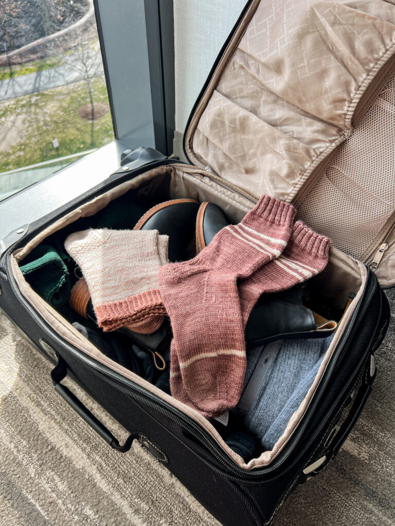 Two pairs of pink, hand-knit socks sitting in the top of an open suitcase.