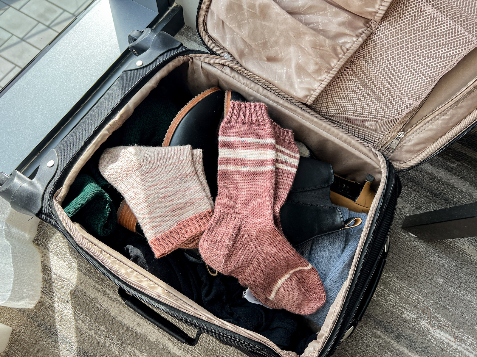 Two pairs of pink, hand-knit socks sitting in the top of an open suitcase.
