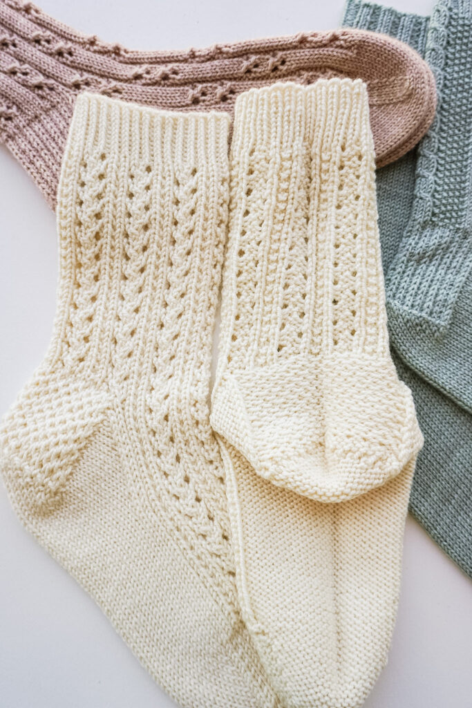 A close-up on the heels of a pair of cream-colored handknit socks. One sock is turned inside-out to show how the slipped stitches in the heel create extra cushioning. The other sock is right-side out to show the Eye of Partridge heel texture.