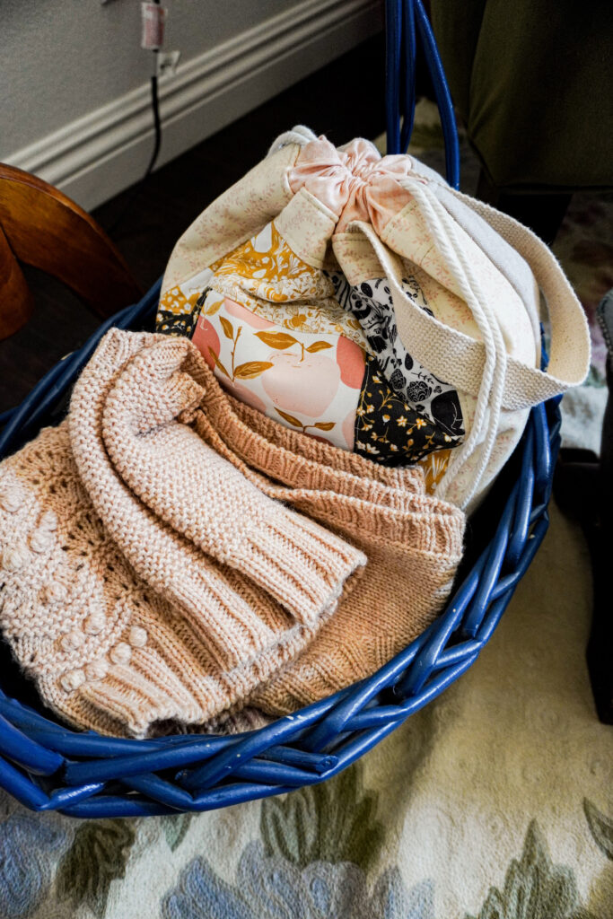 A blue basket with a project bag and some in-progress knitting in it.