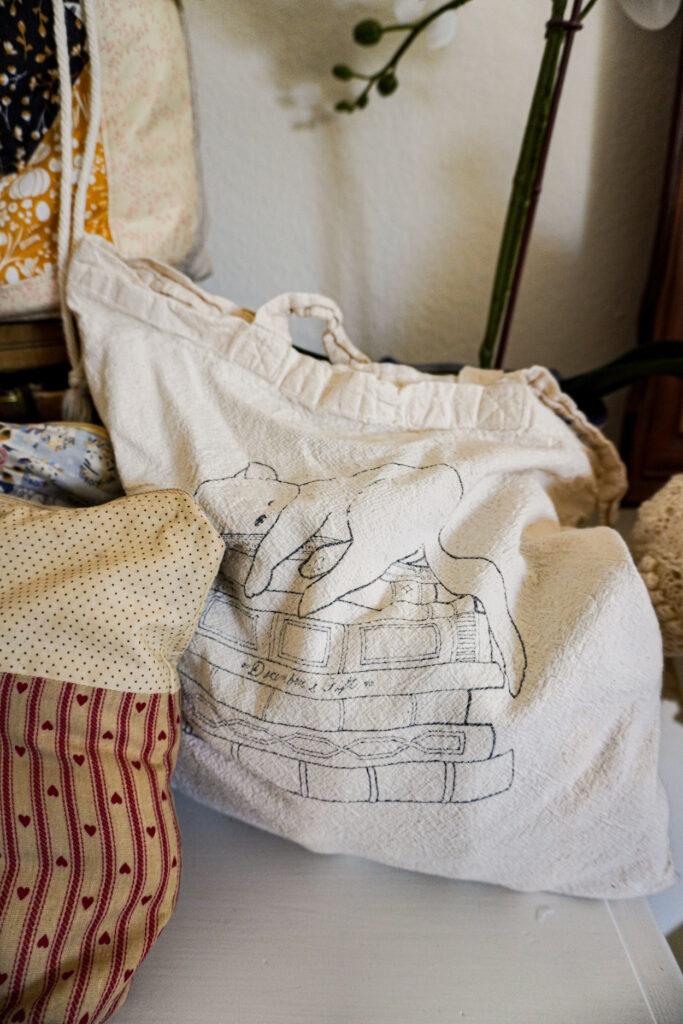 A close-up on a beige canvas bag. There is a line drawing of a kitty sleeping on a stack of books printed on the bag.