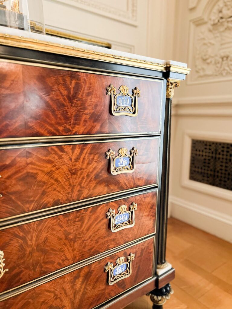 A neoclassical chest of drawers with mahogany drawer fronts and ebony trim. Each drawer handle has a small blue and white plaque embellishment above it. The plaques look like Jasperware from afar, but up close, they're different.
