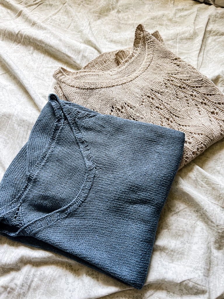 Two folded knit tops--one blue, one tan--sit on a fabric background. The blue one is plain stockinette with a scooped neckline, and it's knit from pure silk yarn. The tan one has a round collar and a round yoke with lace detail, and it's knit from pure linen yarn.