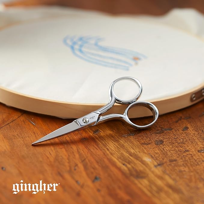 A small pair of silver embroidery scissors leans against the edge of an embroidery hoop.