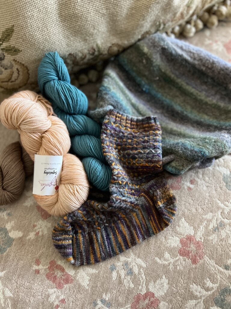 A pile of yarn with a felted striped purse and a knit sock with some minor felting.