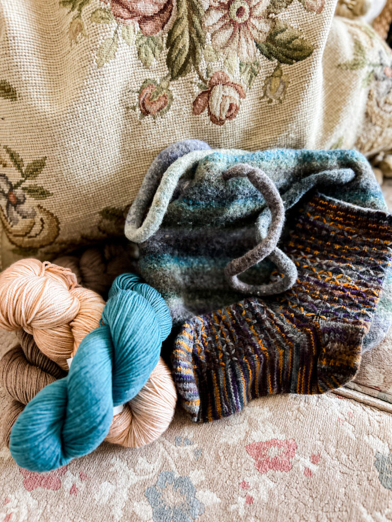 A pile of yarn with a felted striped purse and a knit sock with some minor felting.