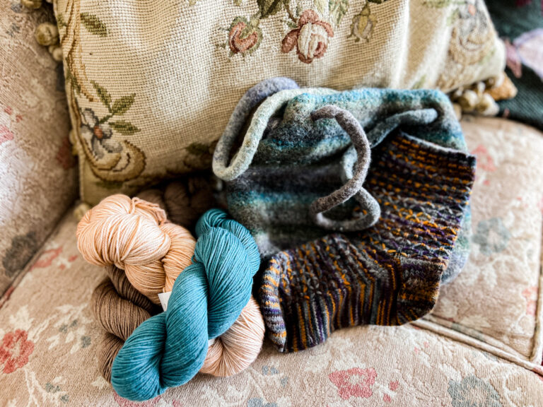 A pile of yarn with a felted striped purse and a knit sock with some minor felting.