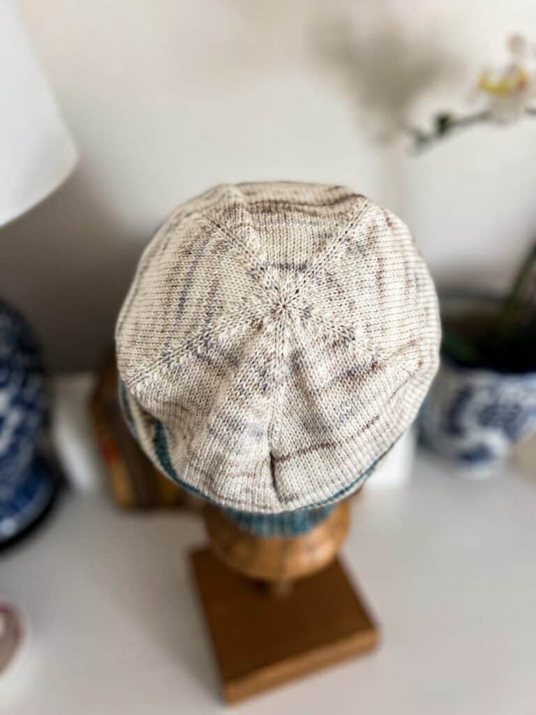 A close-up on the white, speckled crown of a handknit hat showing how the decrease lines converge along five spokes.