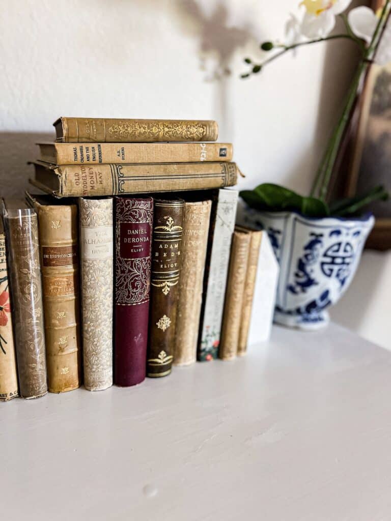 A row of upright antique books with gilded spines sitting on top of a white dresser. A few more books are stacked on top on their sides (don't do this!).