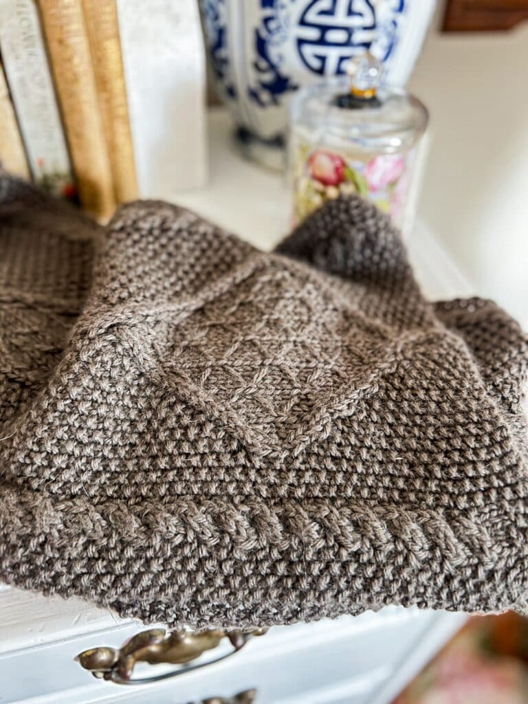 A close-up on a knit scarf with lots of cables and seed stitch. This photo shows the moderate stitch definition in alpaca yarn.