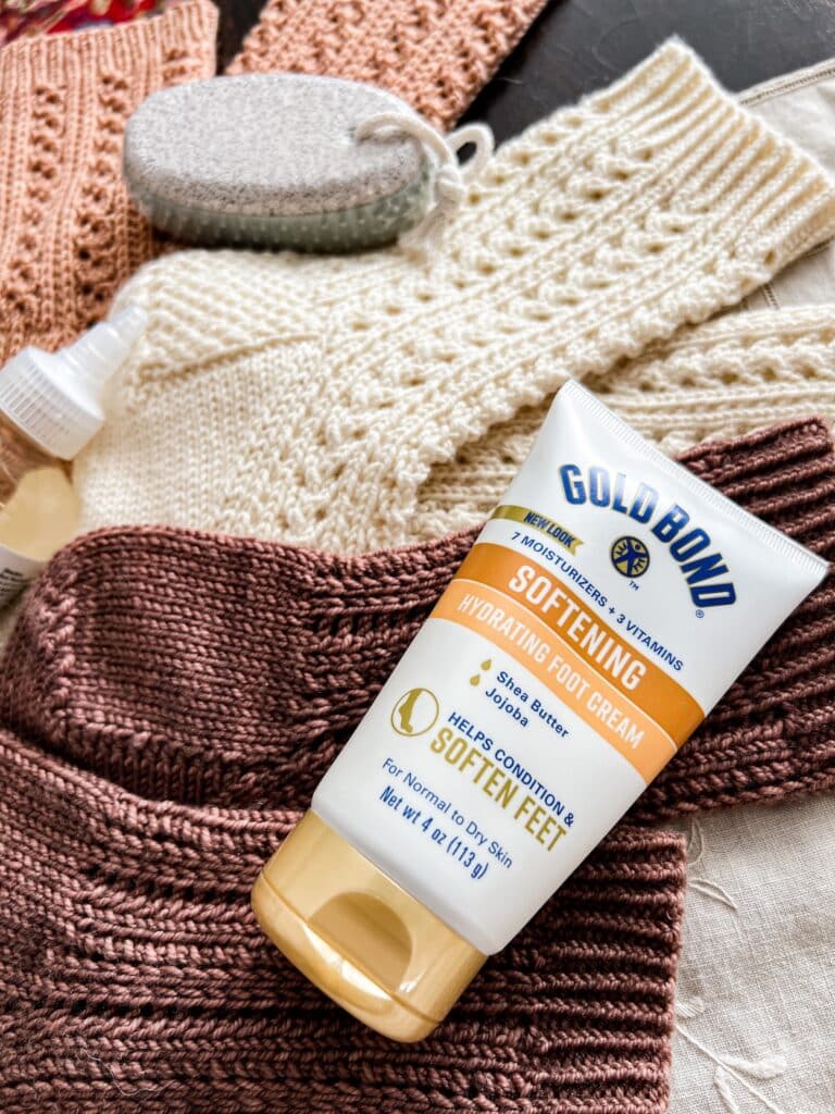 A close-up on a tube of foot moisturizing lotion sitting on top of some brown and white handknit socks.