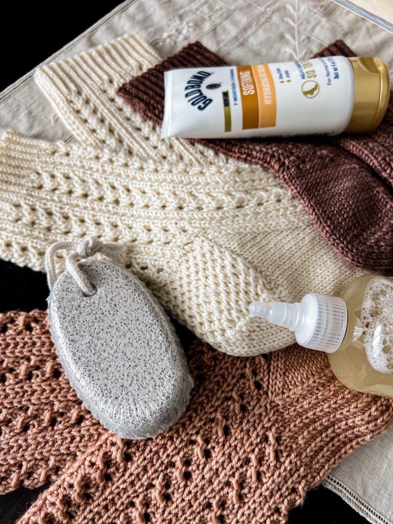A close-up on a gray pumice stone with a rope tied through a hole at one end for a handle. The stone sits on top of some pink and white handknit socks.