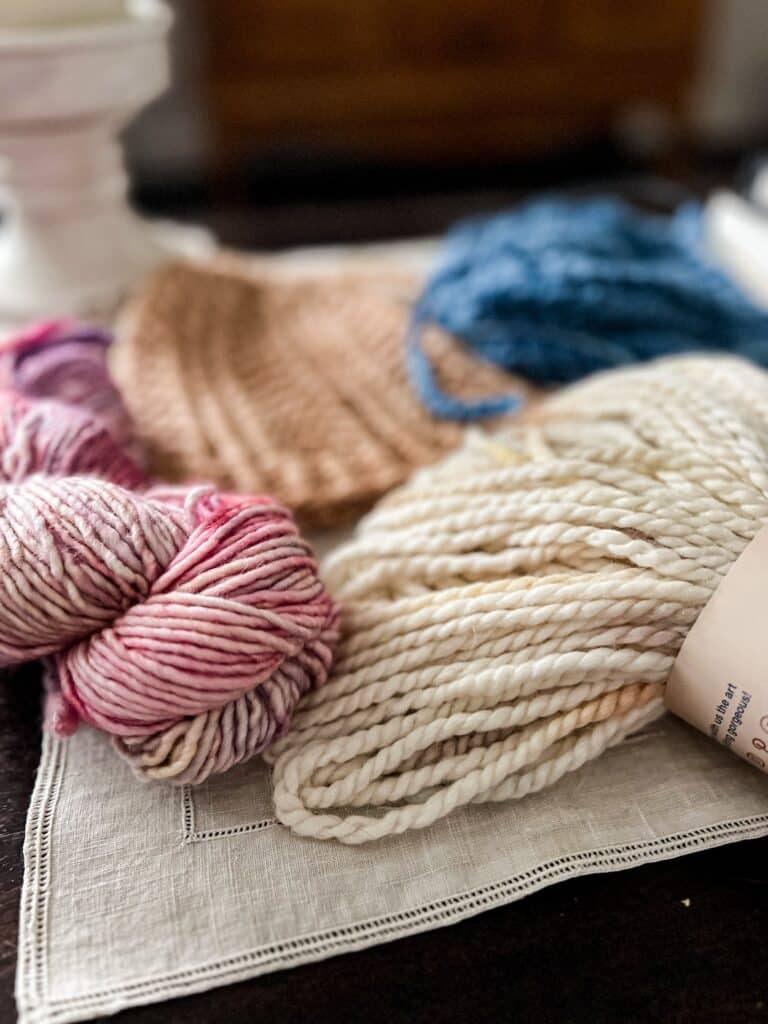 A close-up on two hanks of chunky yarn. The pink yarn on the left is a single-ply yarn from Malabrigo, while the creamy yarn with pastel speckles on the right is a two-ply yarn from Misti Alpaca.