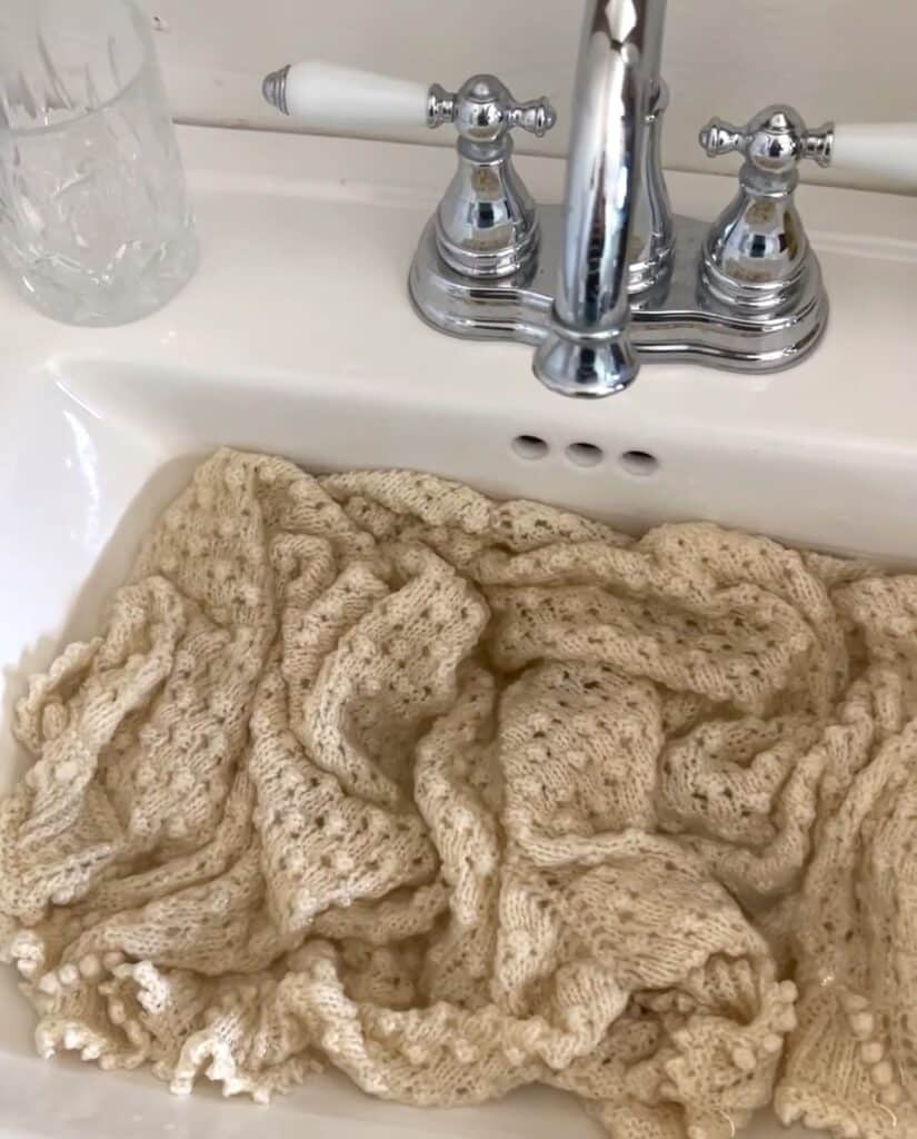 A white knit shawl soaks in a sink full of cool water.
