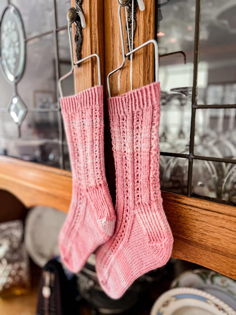 A pair of pink socks hangs from wire sock blockers suspended on the knobs of a vintage oak china hutch.