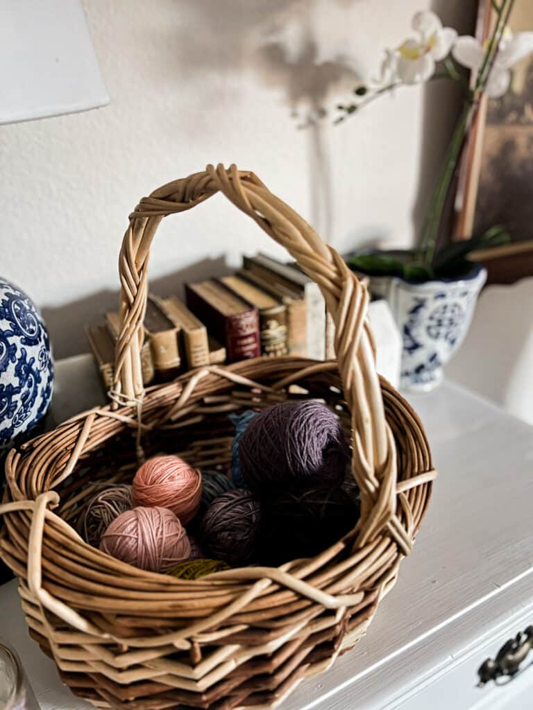 A wicker basket of yarn balls sits on top of a white dresser.