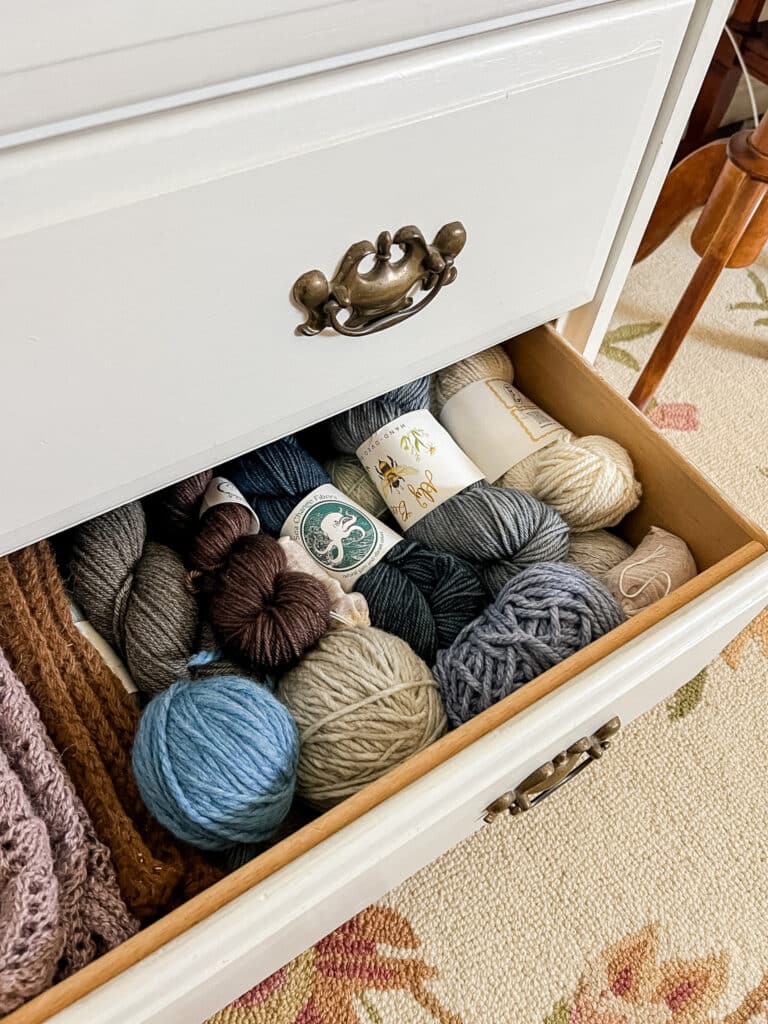 An open drawer of a white dresser holds lots of yarn in hanks and balls.
