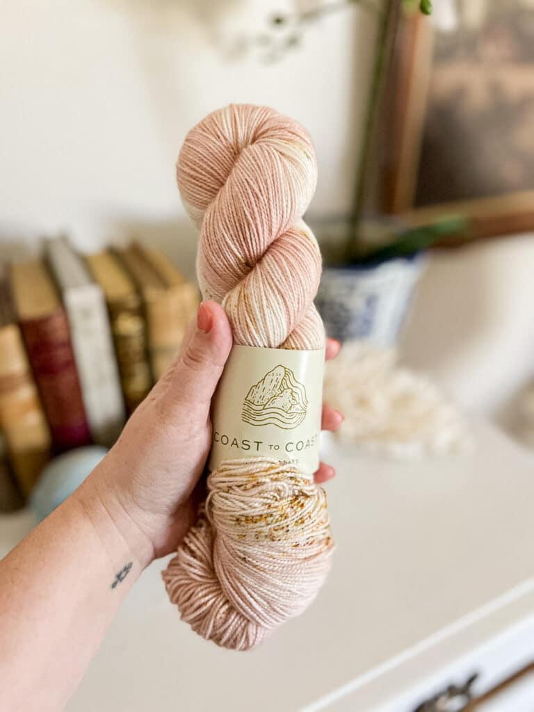 A white woman's left hand holds a hank of yarn.