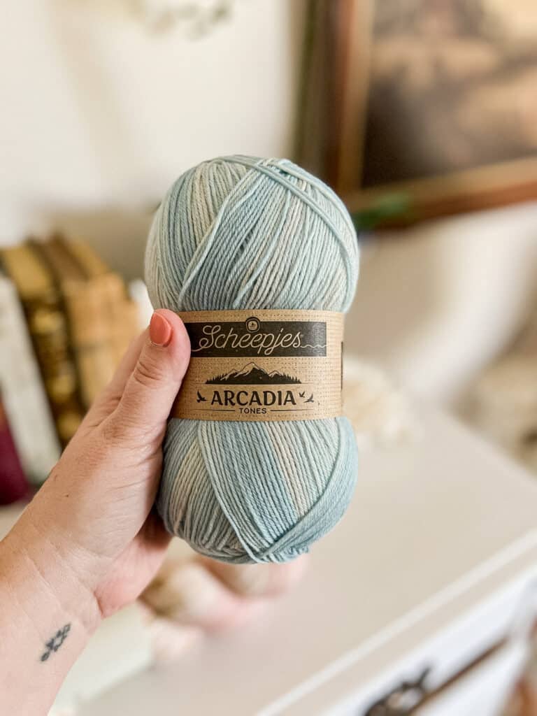 A white woman's left hand holds a skein of yarn.