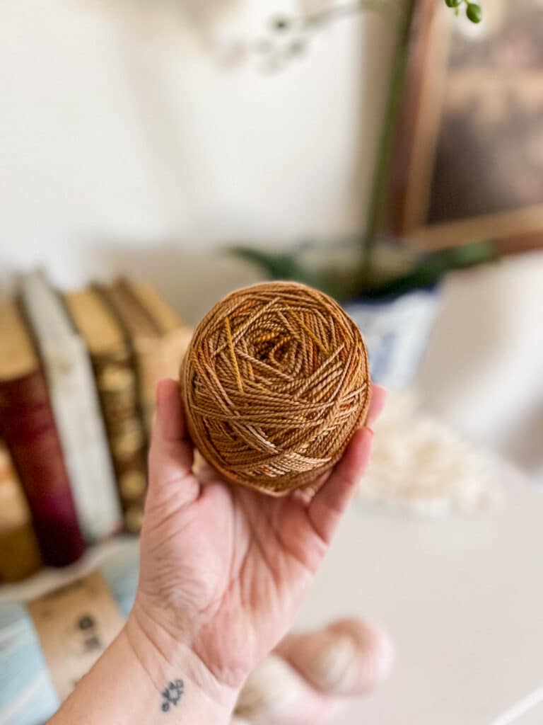 A white woman's left hand holds a cake of yarn.