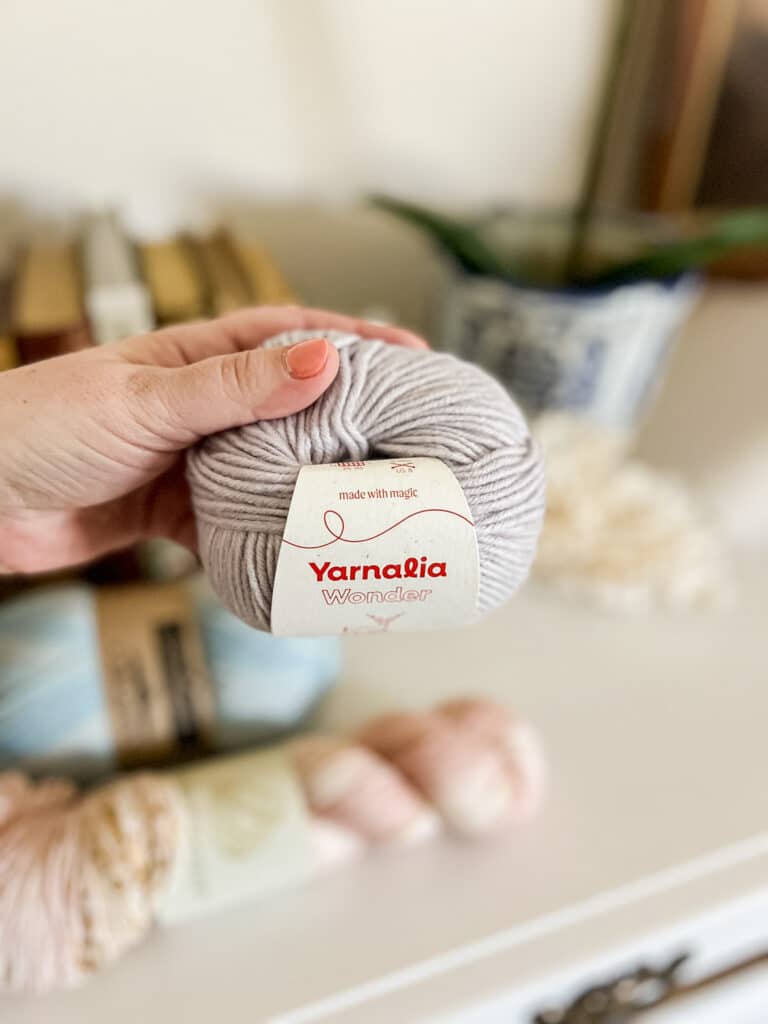 A white woman's left hand holds a lavender ball of yarn.