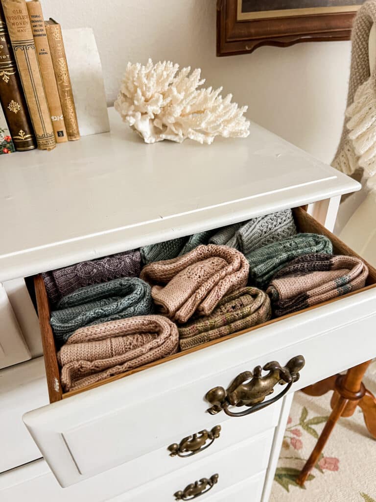 A small drawer on a white dresser is pulled open to display several pairs of neatly folded handknit socks.