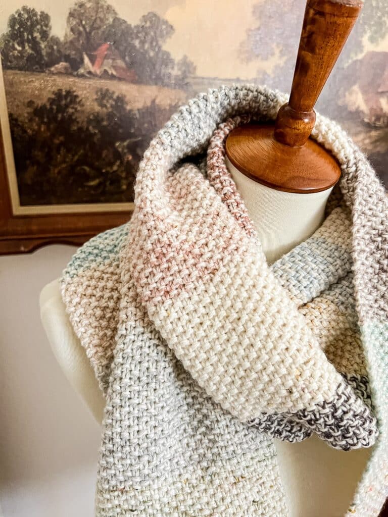 A close-up on the texture of a multicolored seed stitch scarf draped around the neck of a white dressmaker's form.