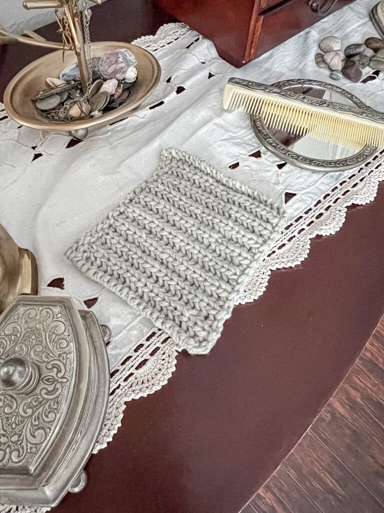 A large, gray swatch of fisherman's rib sits on a dark wood dresser surrounded by vintage trinkets and pretty pebbles from the beach.