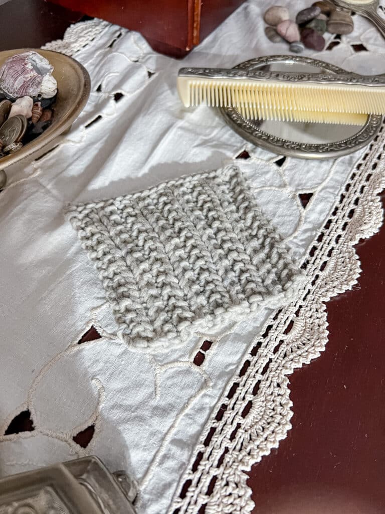 A large, gray swatch of mistake rib sits on a dark wood dresser surrounded by vintage trinkets and pretty pebbles from the beach.