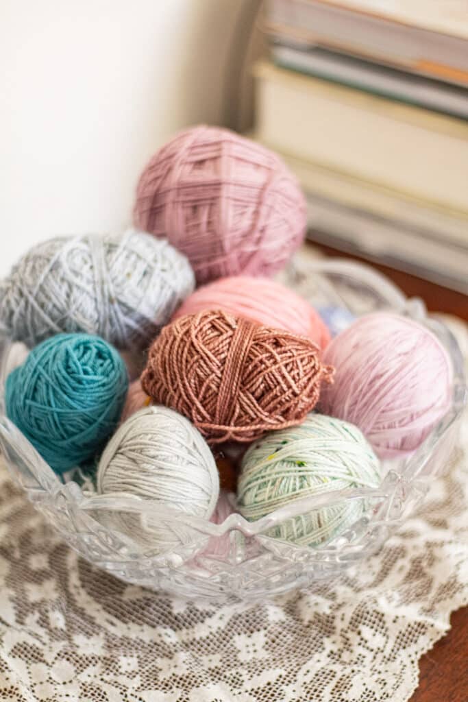 A crystal bowl filled with lots of small remnants of yarn sits on a white doily.