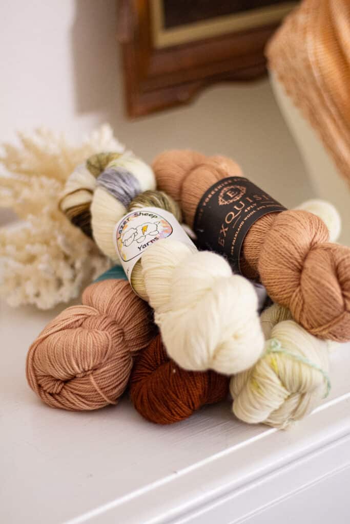 A pile of pink, white, and dark brown hanks of yarn sits on top of a white dresser. This photograph is taken from a low side angle and focuses on the ends of the hanks.