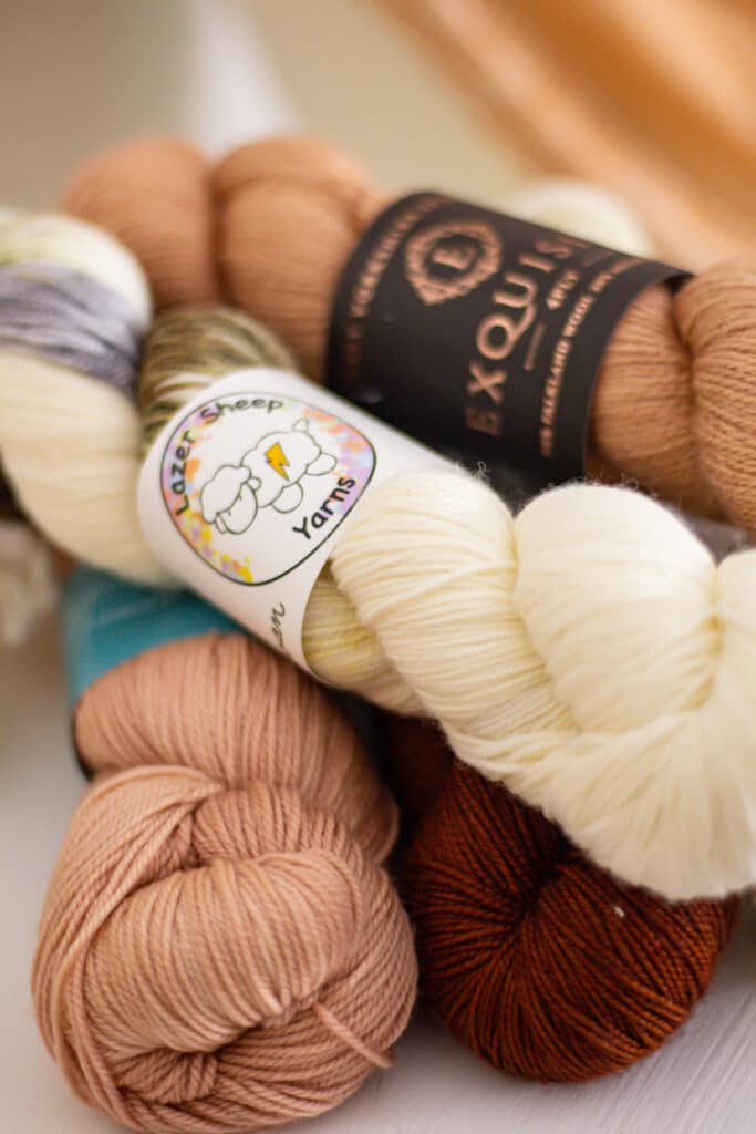 A close-up on a pile of pink, white, and dark brown hanks of yarn sitting on top of a white dresser.
