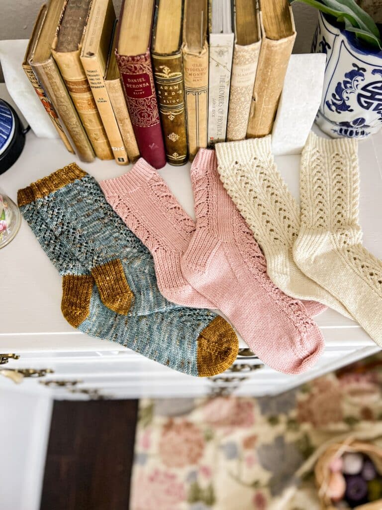 Three pairs of handknit socks are laid out on top of a white dresser. The toes are all pointing to the right and the various socks are overlapping.