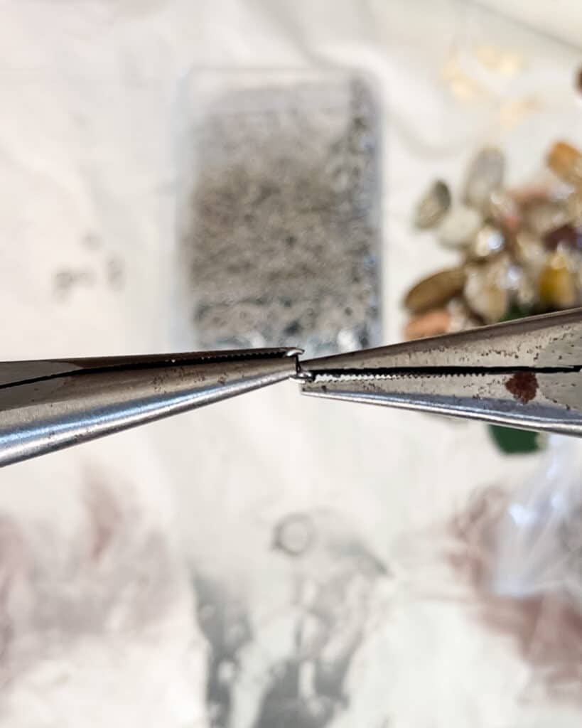 A close-up on a pair of needle nose pliers twisting open a jump ring.