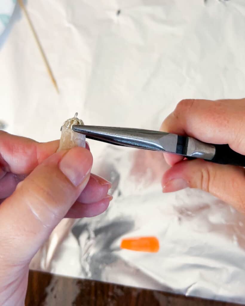 A close-up on a white woman's hands using a pair of needle nose pliers to bend the prongs on a pendant into place.