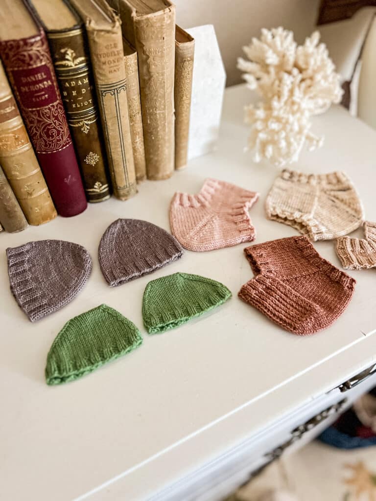 Swatched toes and heels of socks in different shades of pink, purple, and green are laid out on top of a white dresser.