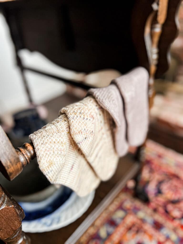 Four knit socks with Eye of Partridge Heels are draped over the towel bar of a vintage tea cart.
