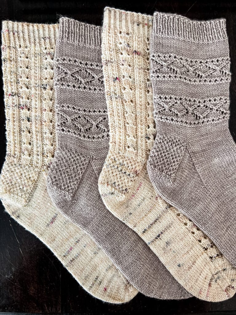 Four socks with Eye of Partridge Heels are laid out flat on a dark wood table. The toes are all pointing to the right.