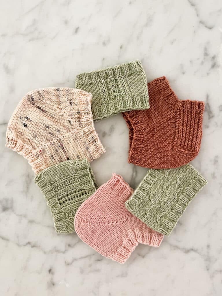 A ring of knit swatches in shades of pink and green sits on a white marble countertop. Some are swatches for sock heel toes, while others are swatches for the backs of fingerless mitts.