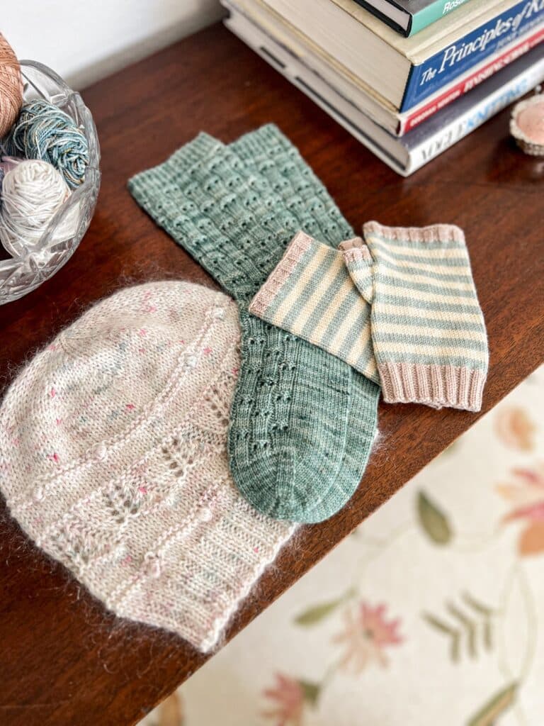 A handknit hat, pair of mitts, and pair of socks rest together on a dark wood table.